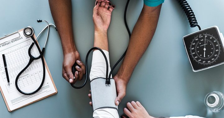 A clinician measuring a patient's blood pressure with an arm cuff and dial gauge, seen from above