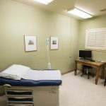 An exam room at a community health center with an exam table, desk and chair