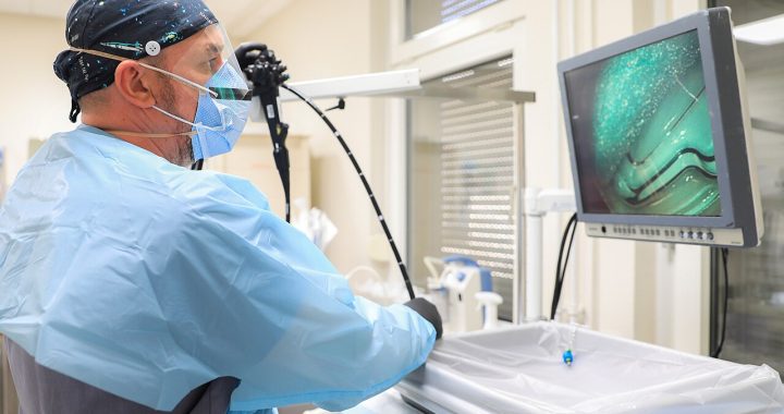 A gastroenterologist holding an endoscope beside a monitor in a procedure room