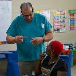 A clinician in teal scrubs talking with a patient in a community clinic